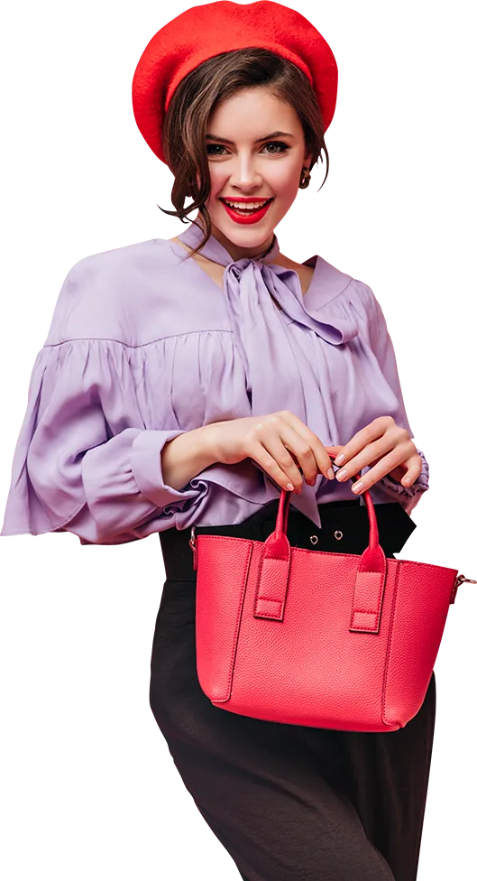 A stylish woman in a purple shirt and black pants holds a red purse, wearing a red hat, showcasing her fashionable look.